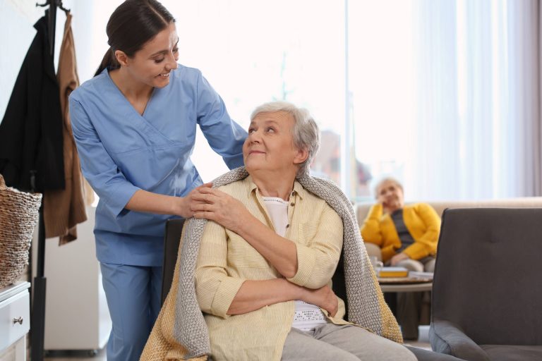 Una cuidadora acompaña a una persona de avanzada edad y se sonríen con amabilidad